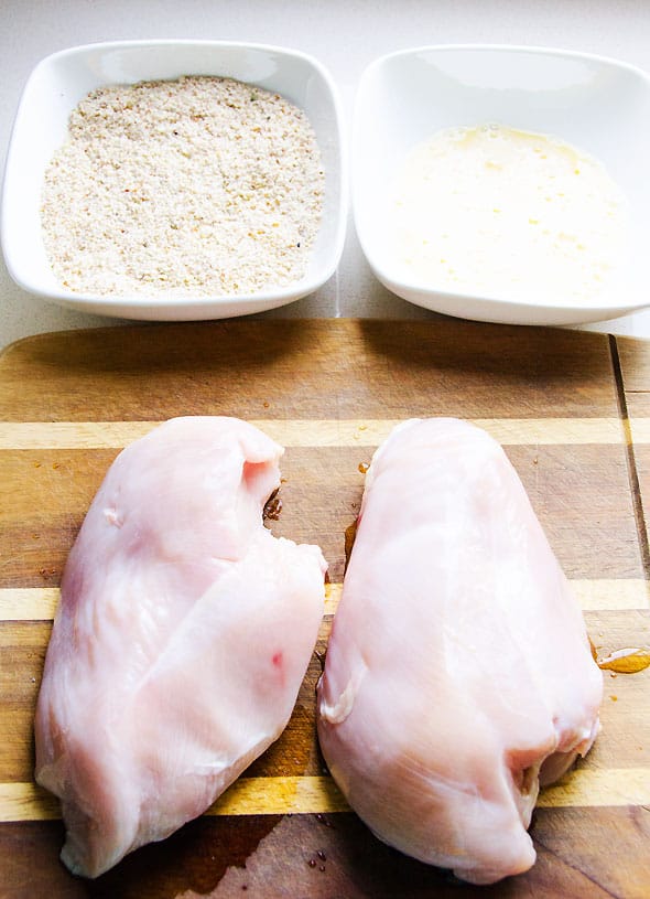 bowls of almond breading and whisked eggs beside chicken breasts on cutting board