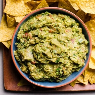 Salsa guacamole in blue bowl on a platter with tortilla chips.