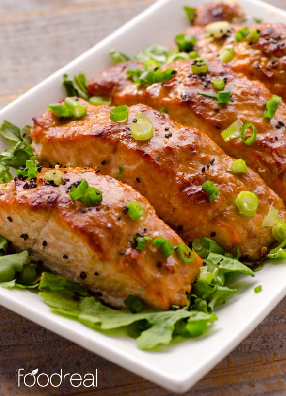 Peanut butter salmon served on a bed of greens and garnished with black sesame seeds and green onions.