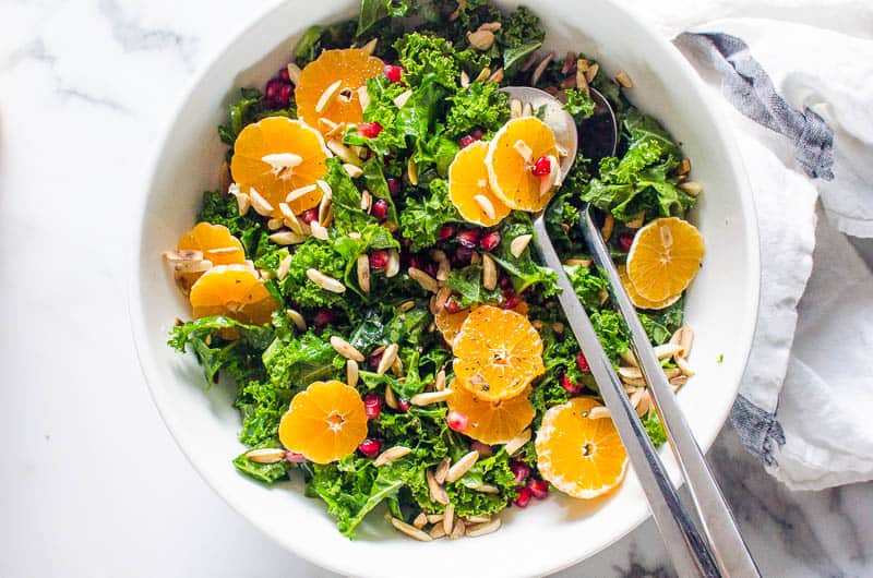 Massaged Kale Salad with mandarins and pomegranate served in a bowl with metal salad spoons