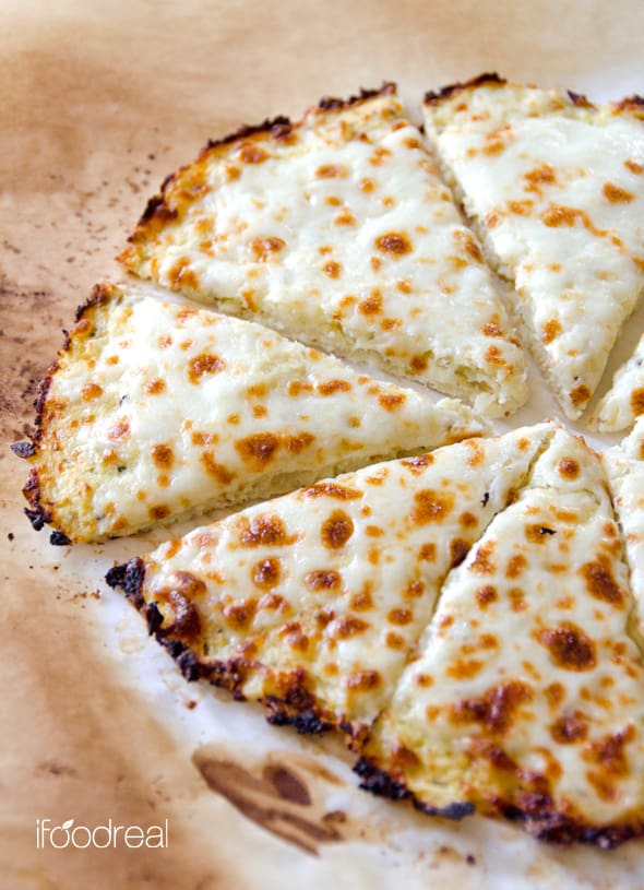 Cauliflower pizza crust with cheese sliced on parchment paper.