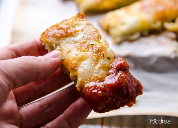 A hand holding a cauliflower breadstick dipped into sauce.