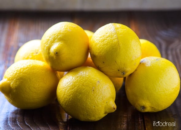 A pile of lemons on a wood surface.
