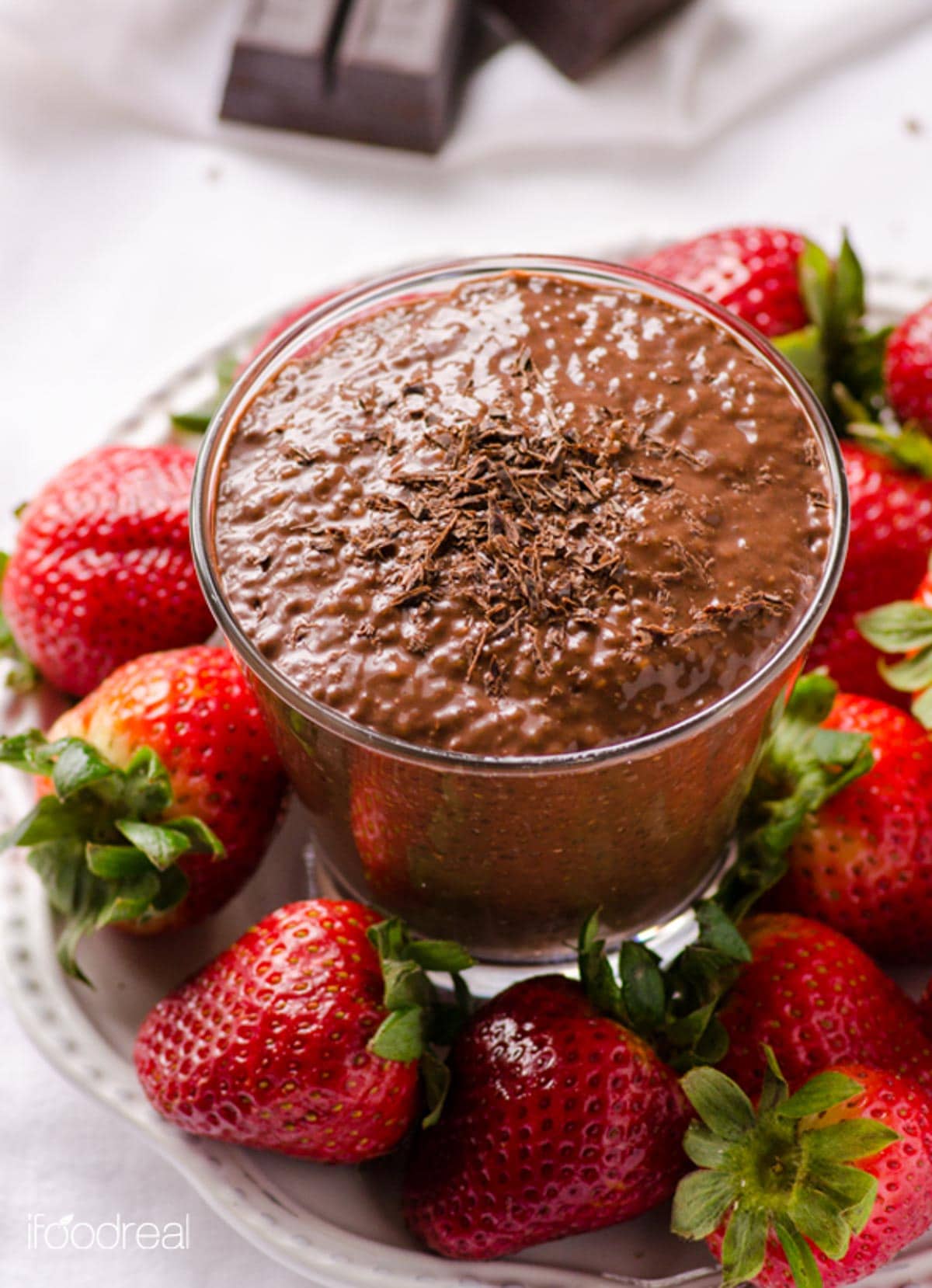 Chocolate chia pudding in a cup on plate with fresh strawberries.