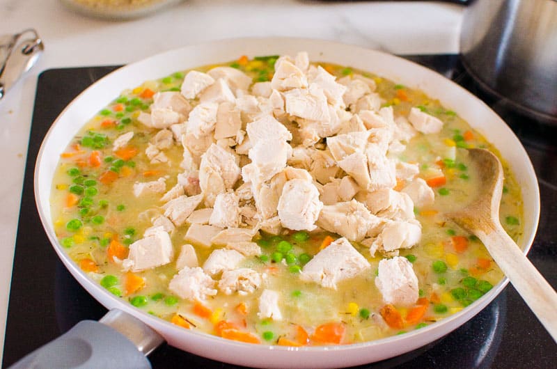 Chicken in a skillet with liquid mixture and vegetables.