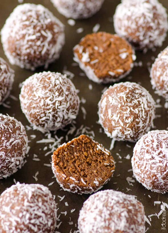 almond joy protein balls with two split open to show chocolate inside and all topped with coconut flakes.