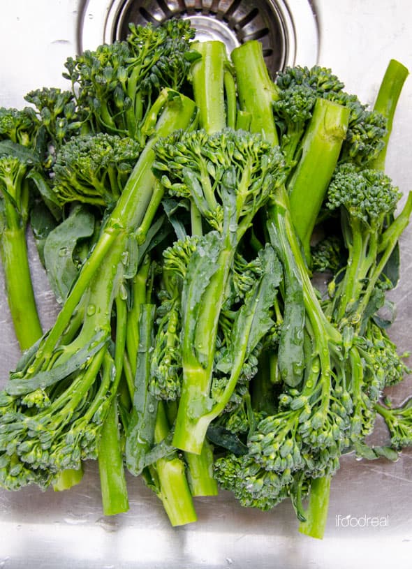 Broccolini being washed in sink.