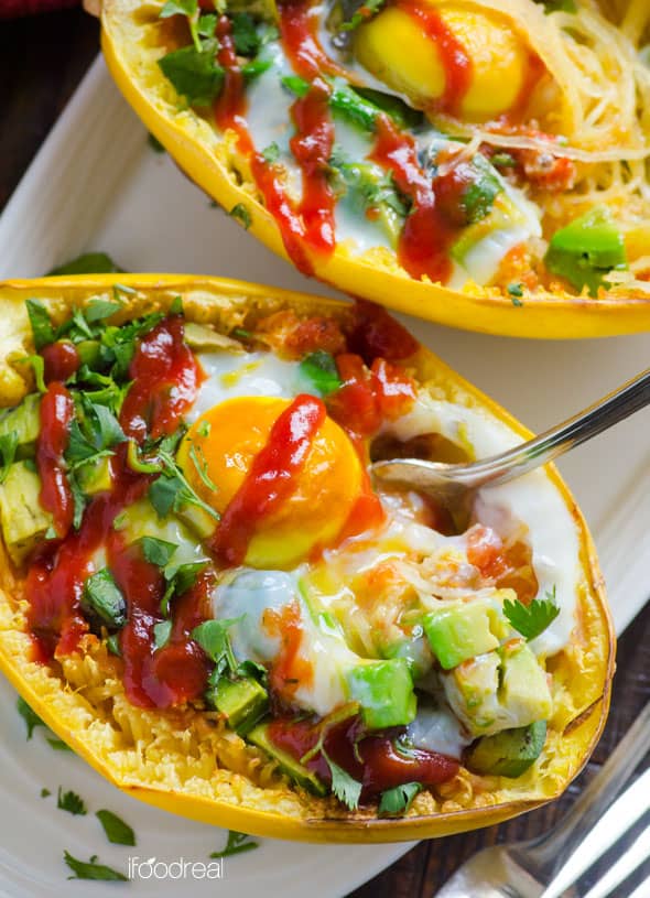 Close up of spaghetti squash as bowls filled with cooked spaghetti squash egg and avocado with cilantro garnish and drizzle of ketchup with a fork. 
