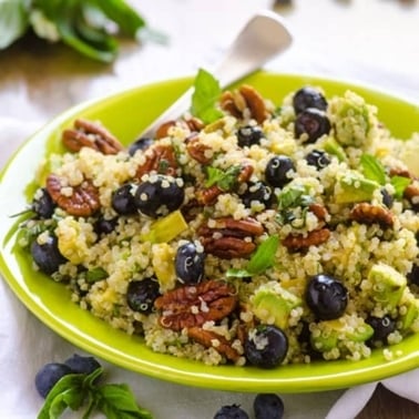 Blueberry quinoa salad with pecans and avocado on a green plate.