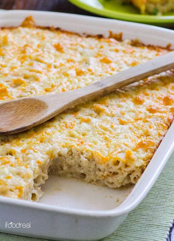Baked mac and cheese with cauliflower in baking dish with one sliced removed and wooden spoon on top.
