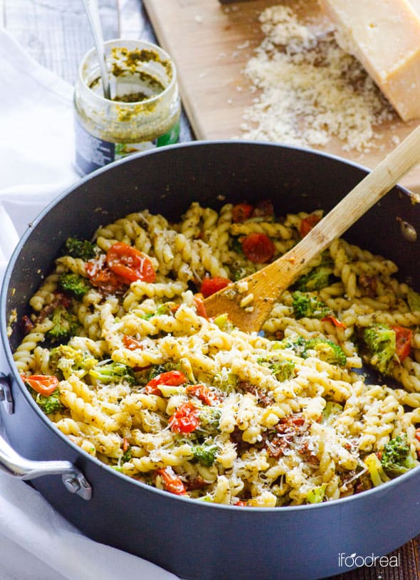 Healthy pasta recipe with tomatoes, broccoli and cheese in a skillet with a spoon.