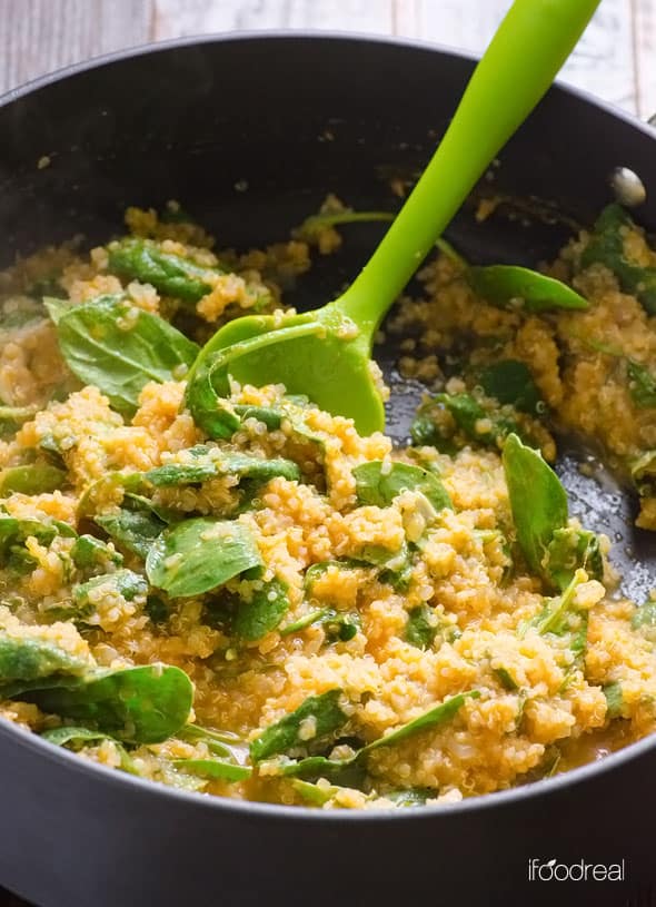 Parmesan pumpkin quinoa with spinach in a skillet with green spatula.