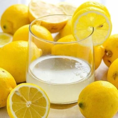 Lemon water in a glass with fresh lemons.