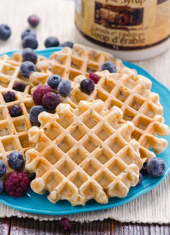 Healthy waffles garnished with frozen berries on a blue plate.