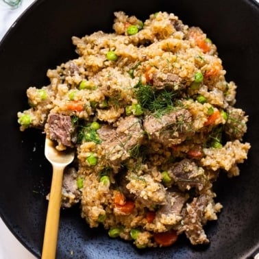 Beef quinoa stew with peas and carrots served in black bowl with a fork.