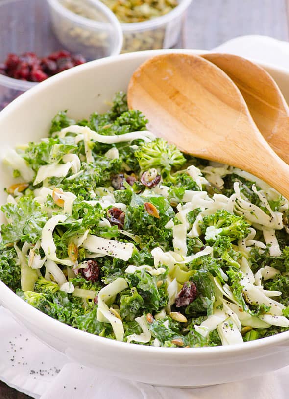 Sweet kale salad in white bowl with serving spoons.