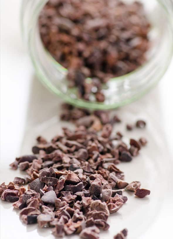 Raw cacao nibs coming out of a jar that is laying on its side.