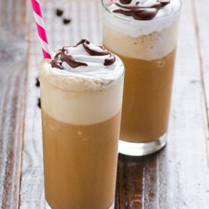 Healthy homemade frappuccino in two glasses with whipped topping, chocolate syrup and straws.