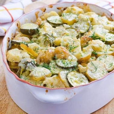 Zucchini potato bake with melted cheese and fresh dill on top served in a baking dish.