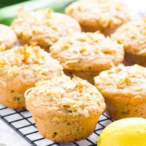 Healthy lemon zucchini muffins on cooling rack with fresh lemon and zucchini.