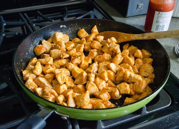 cooking chicken breast with hot sauce in a skillet