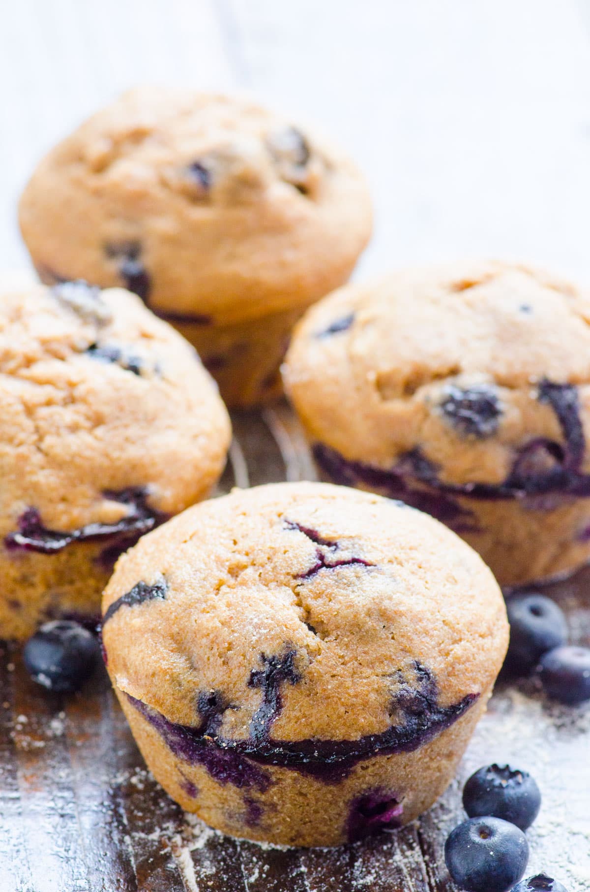 Four healthy blueberry muffins on a counter with fresh blueberries.