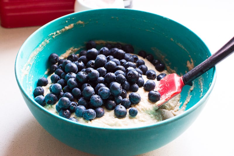 Blueberries and muffin batter in blue bowl with spatula.