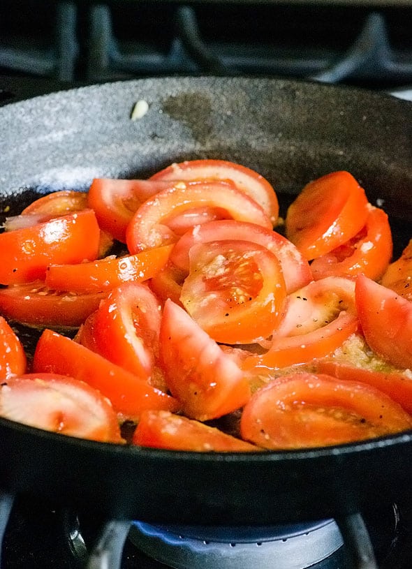 sliced tomatoes in cast iron skillet cooking on a stove