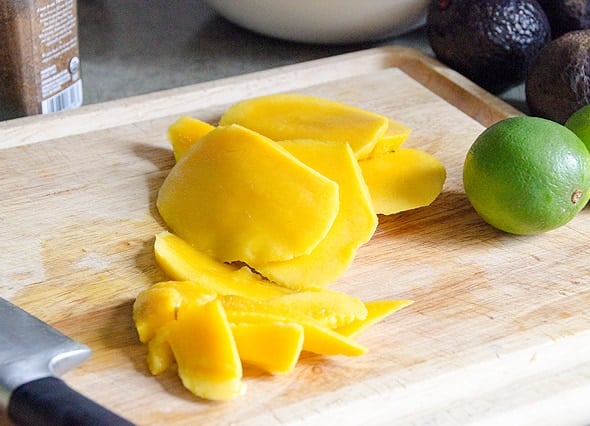 Sliced mango on a cutting board with a lime.