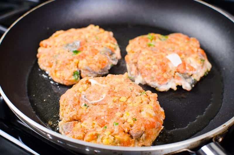 Frying salmon burgers in a skillet on stove.
