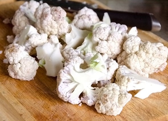 Cauliflower florets on a cutting board with a knife.