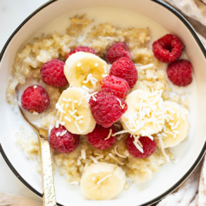 Quinoa breakfast bowl with milk, raspberries, banana and coconut flakes.