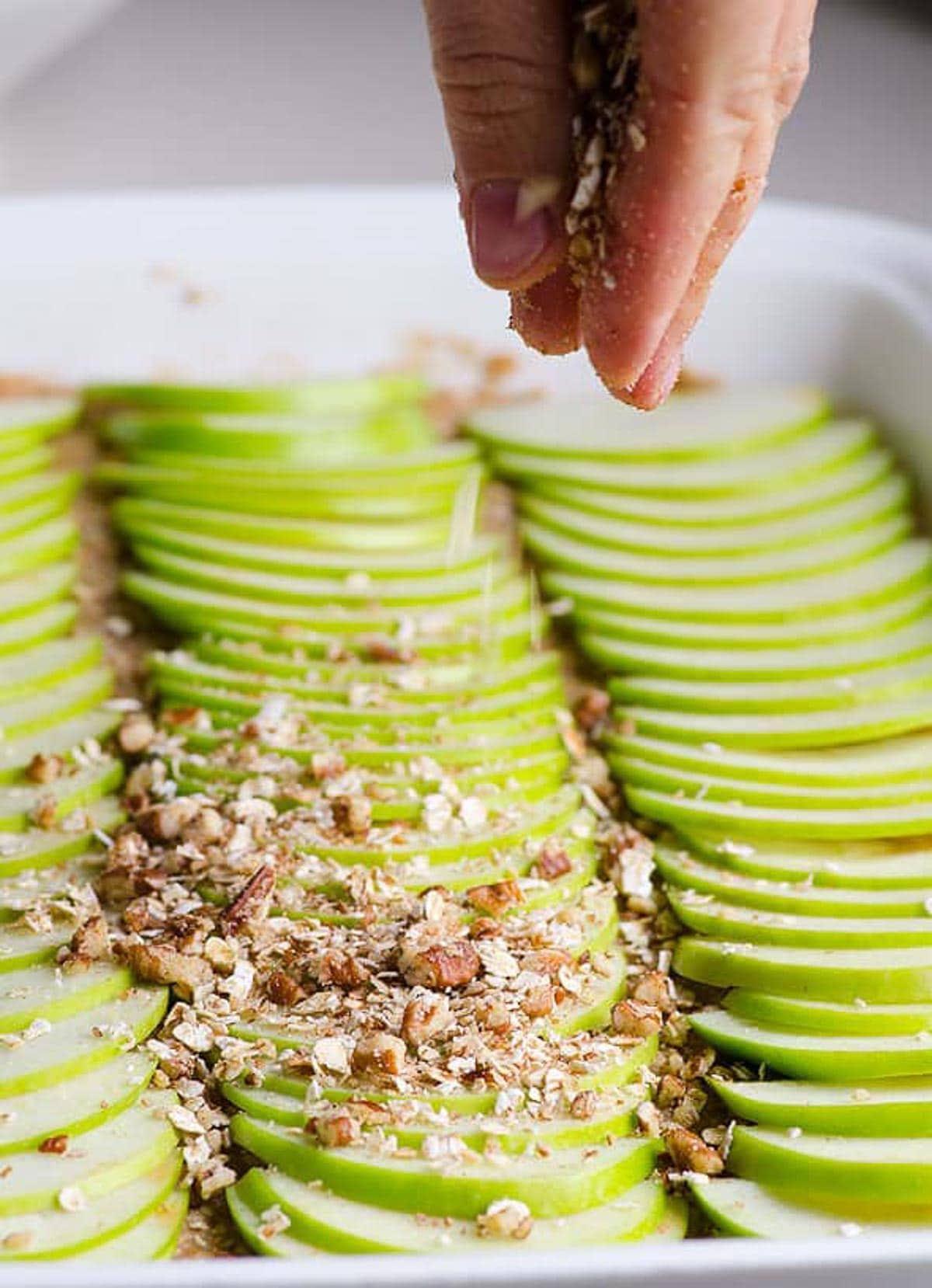 Sprinkling crumb topping over top of sliced apples.