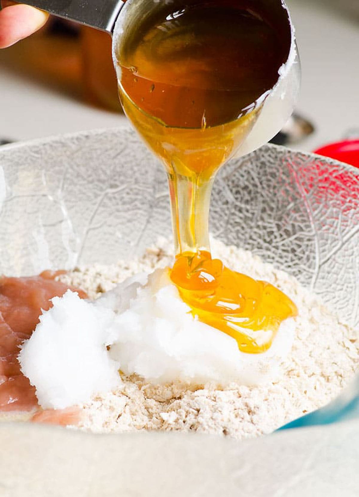 Pouring honey over oats, flour, applesauce and coconut oil in bowl.