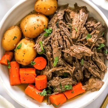 Shredded rump roast served with carrots and baby potatoes in white bowl.