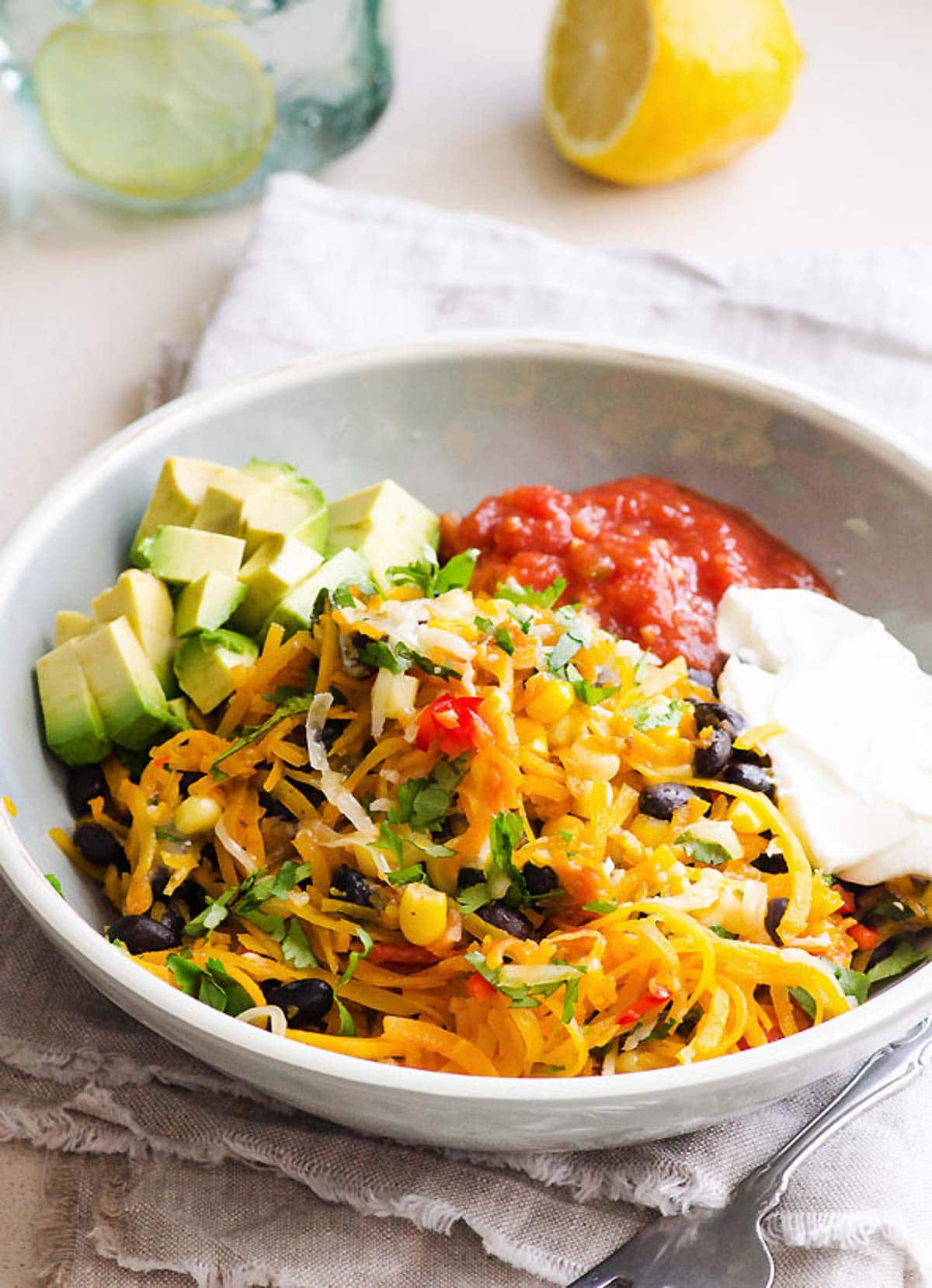 Butternut squash noodles served with salsa, sour cream, avocado and cilantro in a bowl.