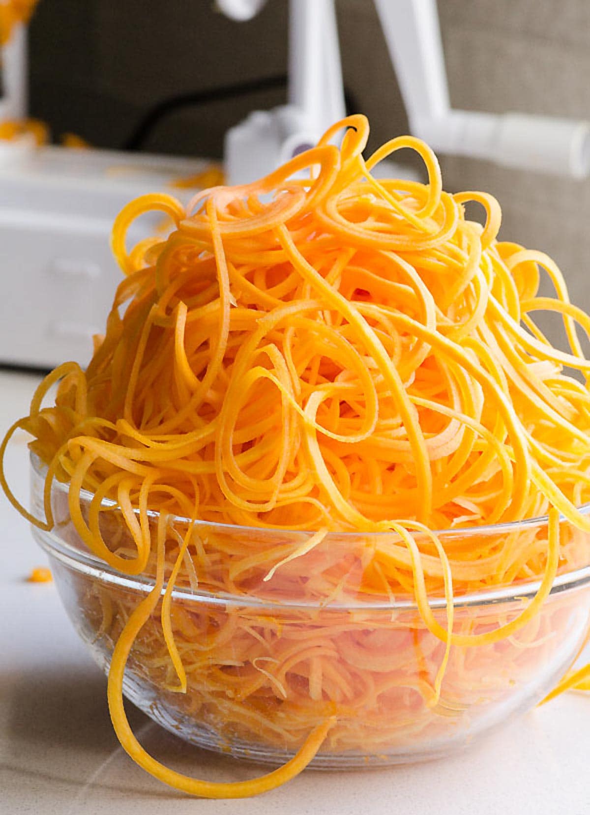 A bowl with butternut squash noodles. Spiralizer behind.