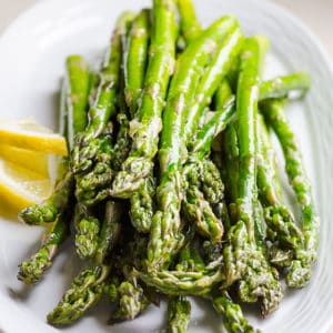 Broiled asparagus with lemon slices on a plate.