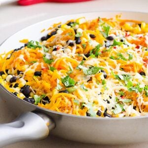 Tex mex butternut squash noodles in a skillet. White spoon on red spoon rest.