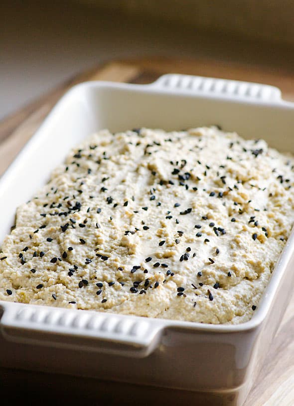 Unbaked quinoa bread in loaf pan topped with black sesame seeds.