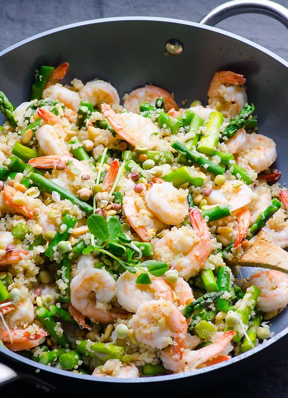 Shrimp, peas, quinoa and asparagus cuts in a skillet.