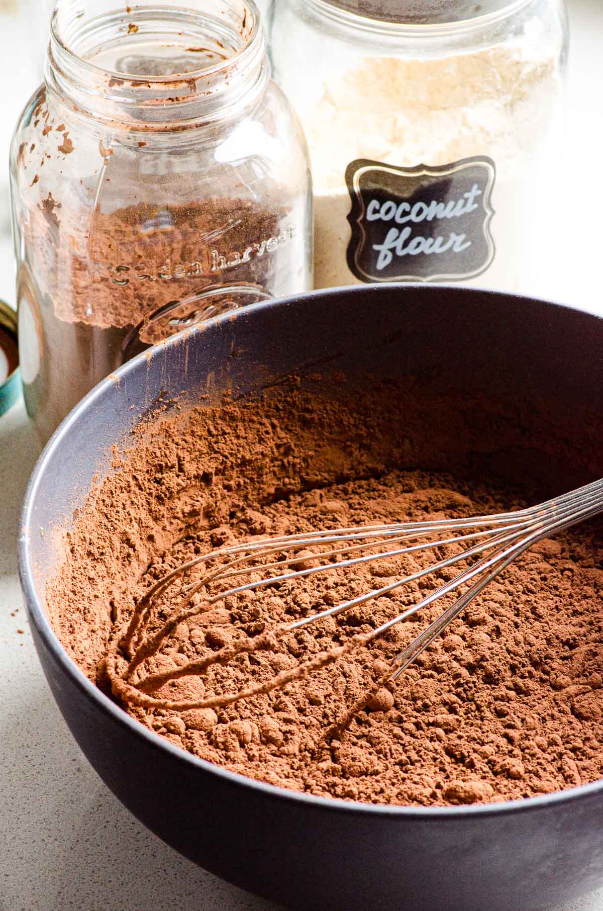 Coconut flour and cacao powder mixed in bowl with a whisk.