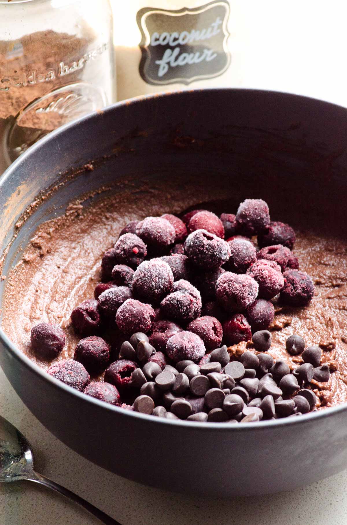 Frozen cherries and chocolate chips on top of batter in bowl.