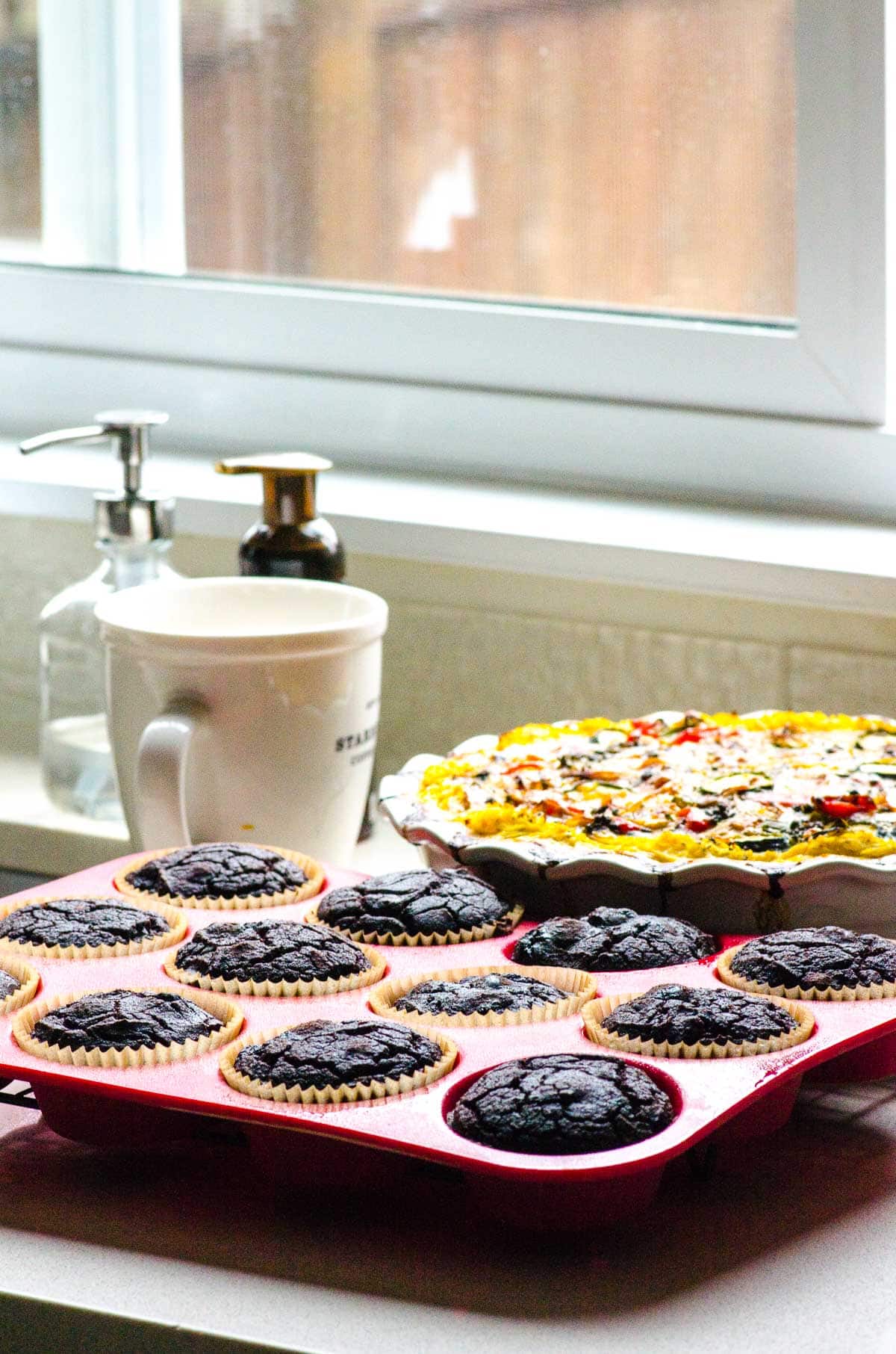 Chocolate coconut flour muffins in muffin tin by the window.