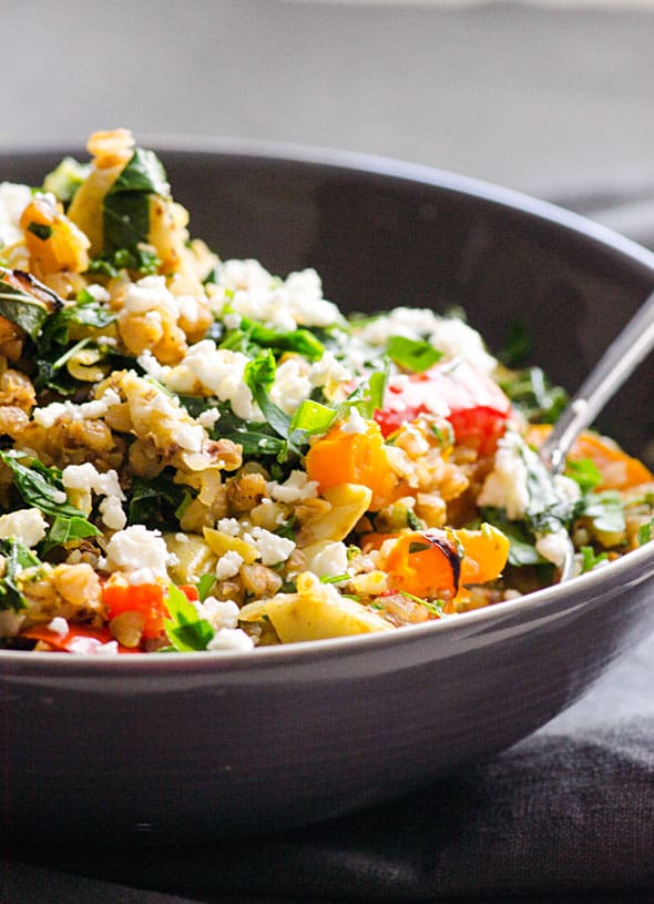 Cooked buckwheat recipe in dark gray bowl with stir fried peppers, kale  and topped with feta cheese.