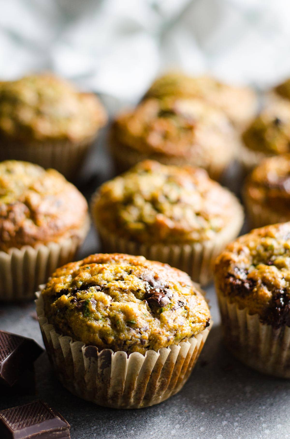 Healthy banana zucchini muffins on a table with chocolate chunks around.