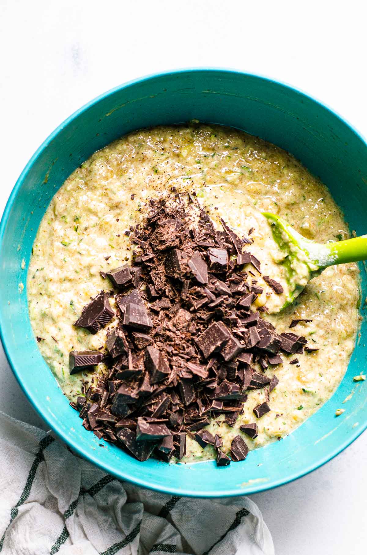 Muffin batter with chopped dark chocolate and spatula in a blue bowl.