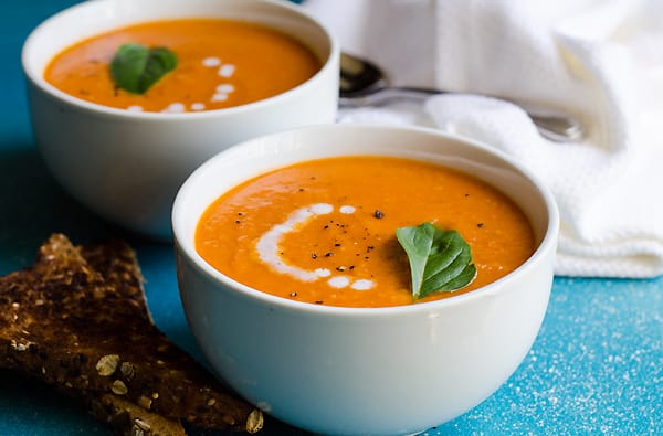 Two white bowls of sundried tomato soup garnished with basil and served with toasts.