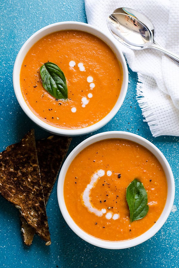 Sun-dried tomato soup served in bowls and garnished with coconut milk and fresh basil.