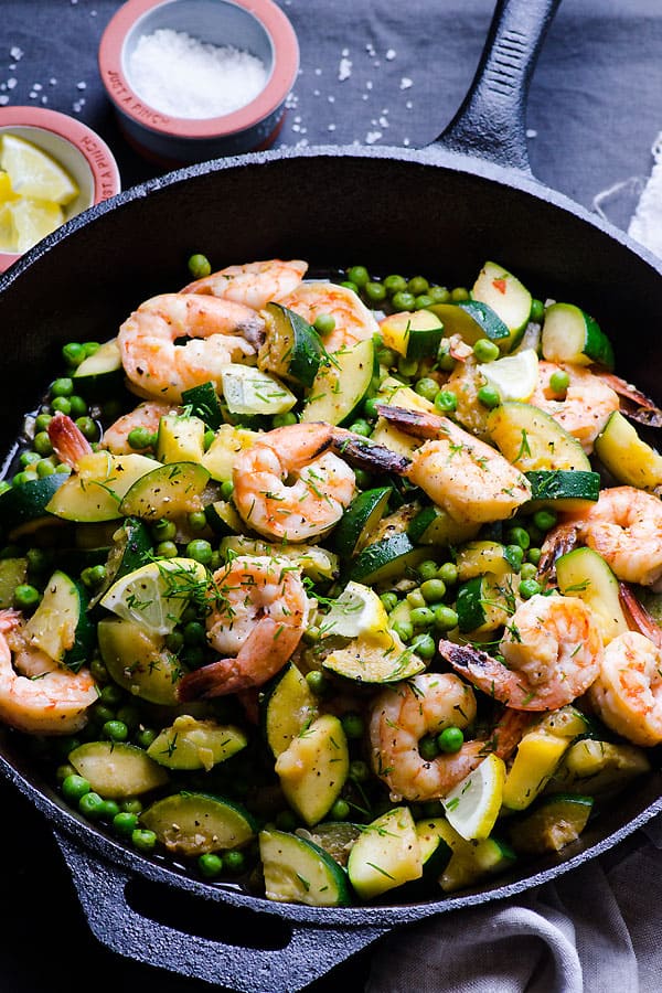 Shrimp zucchini peas and dill with lemon in a skillet.